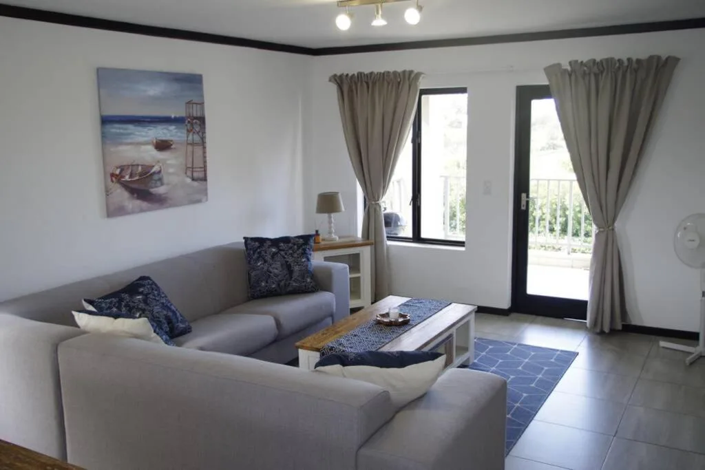 Bright lounge with gray sofas, coastal artwork, and glass doors to deck