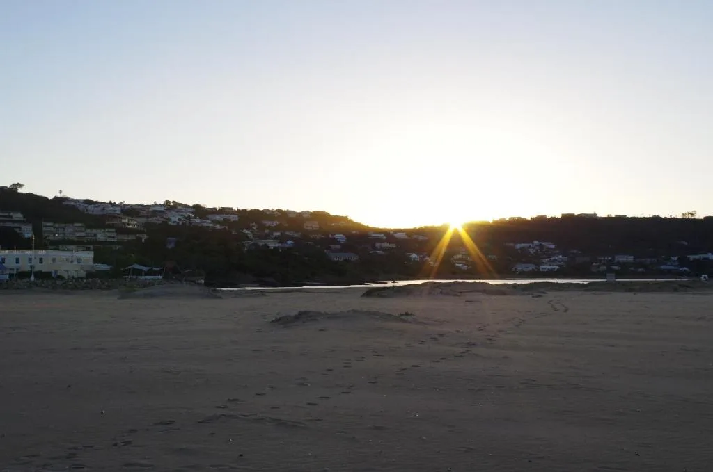 Sunrise over Plettenberg Bay beach with golden light breaking through hills
