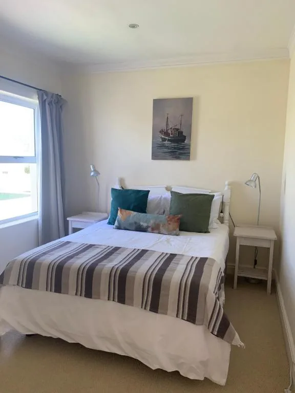 Bright bedroom with queen bed, striped quilt, colorful cushions, and ocean artwork