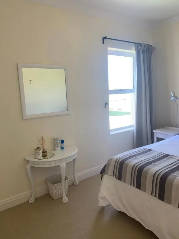 Bright bedroom with striped bedding, vanity table, and glass door to deck