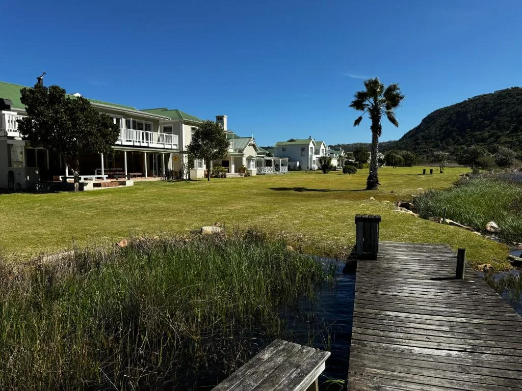 White houses with green roofs overlook expansive lawn and wooden boardwalk