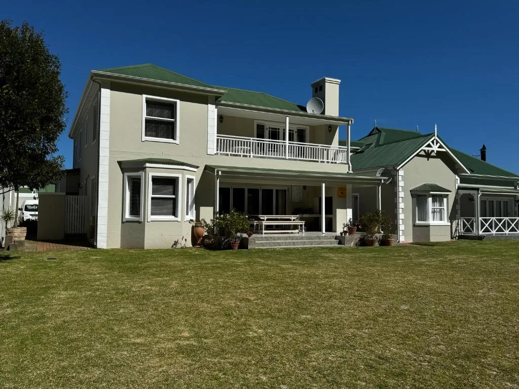 Cream and green historic main house with manicured lawn and clear blue sky