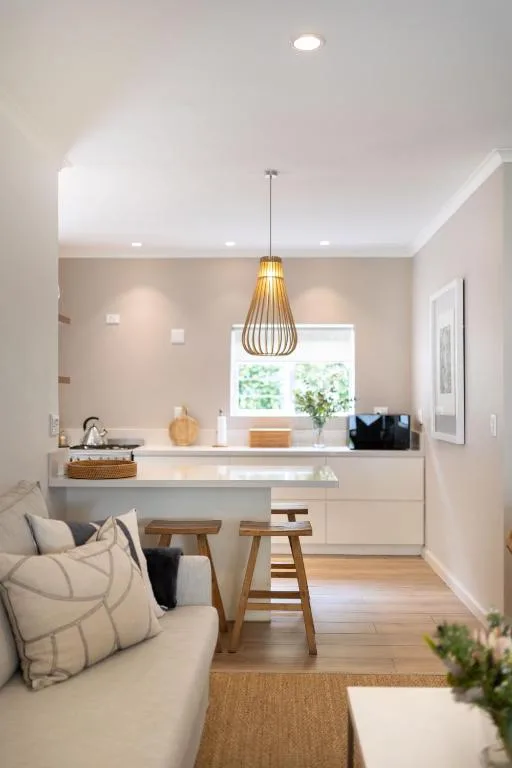 Modern living area with cream sofa, kitchen counter, wooden bar stools