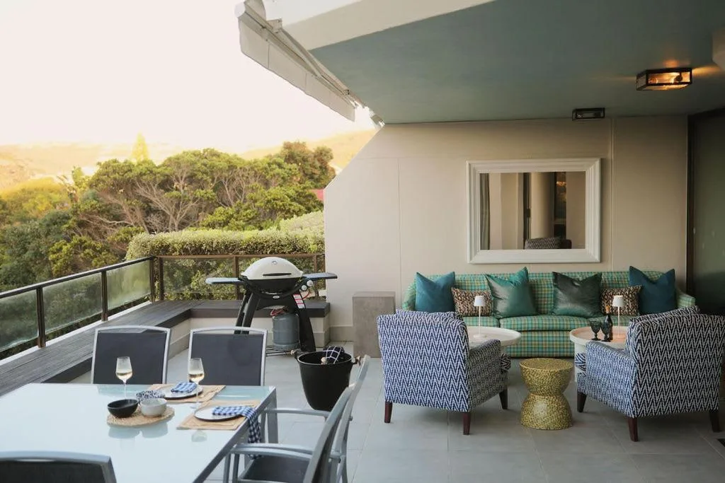 Covered outdoor deck with dining table, seating, braai, and green landscape views