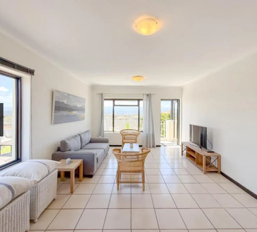 Bright open-plan lounge with sofa, dining area, and scenic views through glass doors