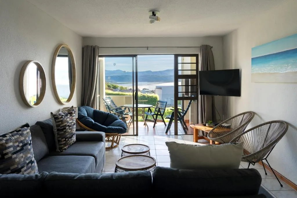 Modern lounge with blue sofa, TV, and panoramic sea views through glass doors