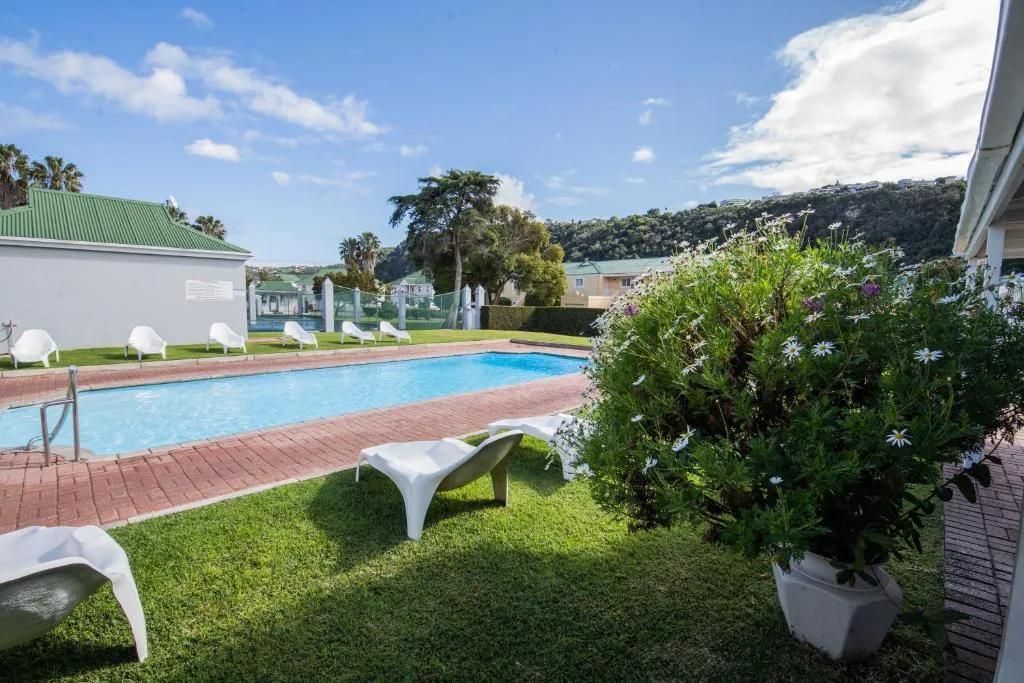 Resort swimming pool with loungers, lush gardens, and waterfront views beyond