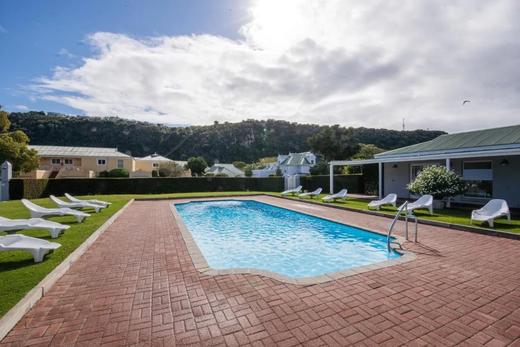 Resort swimming pool with brick patio, loungers, and green lawns