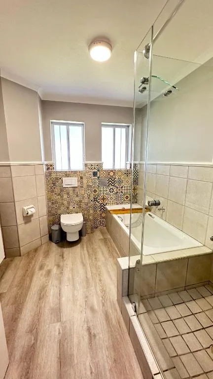 Modern bathroom with glass shower enclosure, toilet, and decorative tile accents