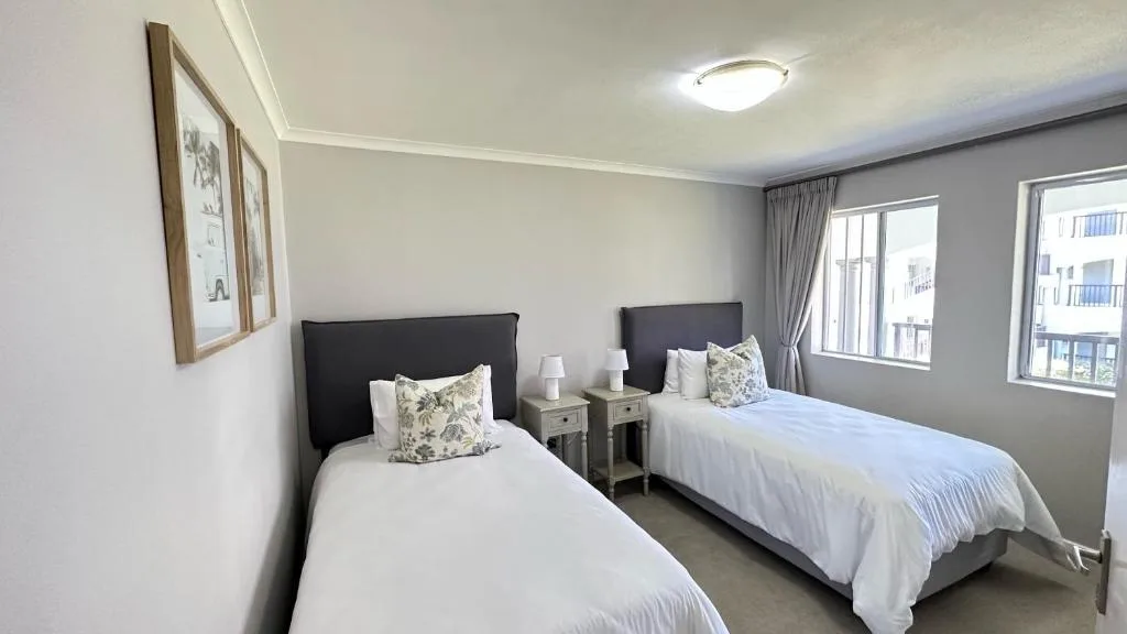 Twin bedroom with white linens, black headboards, and natural light from windows