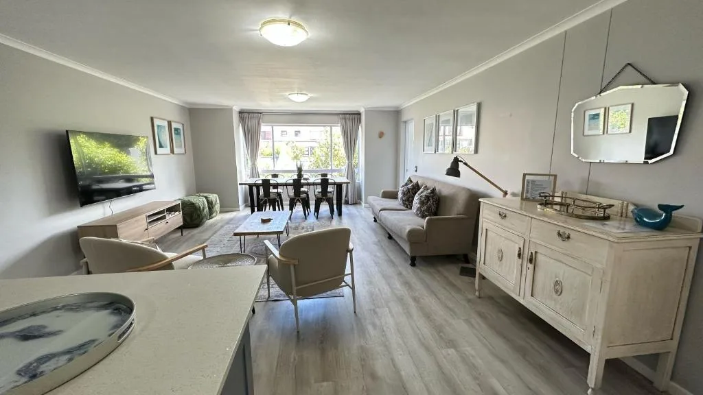 Spacious open-plan lounge with sofa, armchairs, TV, and natural light from windows