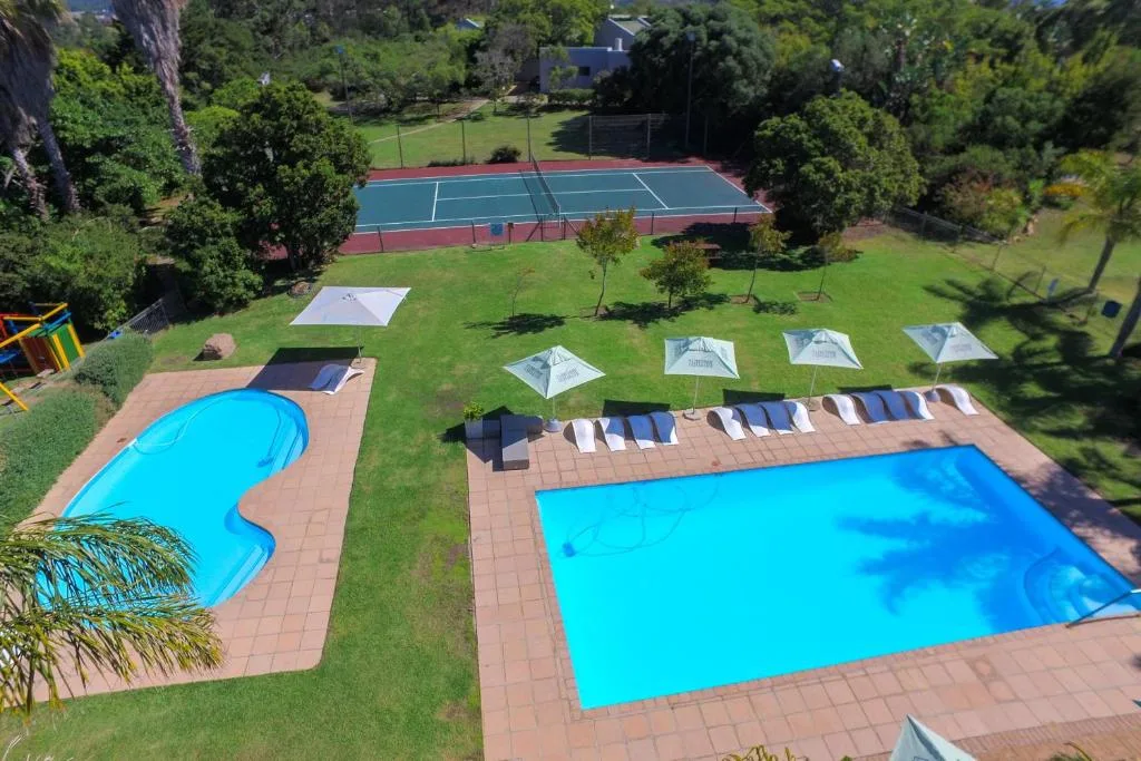 Two bright blue swimming pools with loungers and umbrellas on brick patio