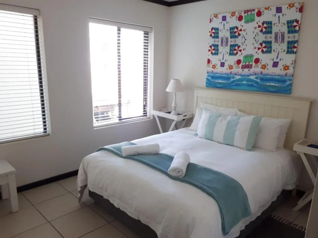 Bright bedroom with queen bed, striped pillows, and beach-themed wall art