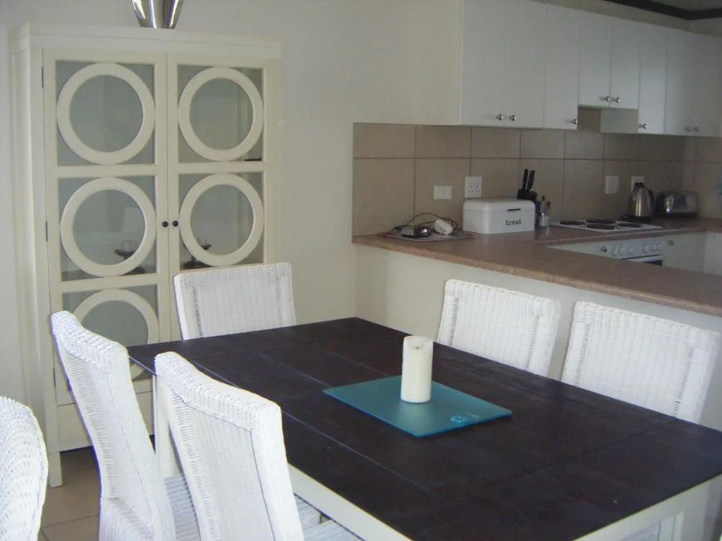 Dining table with white chairs and kitchen in background