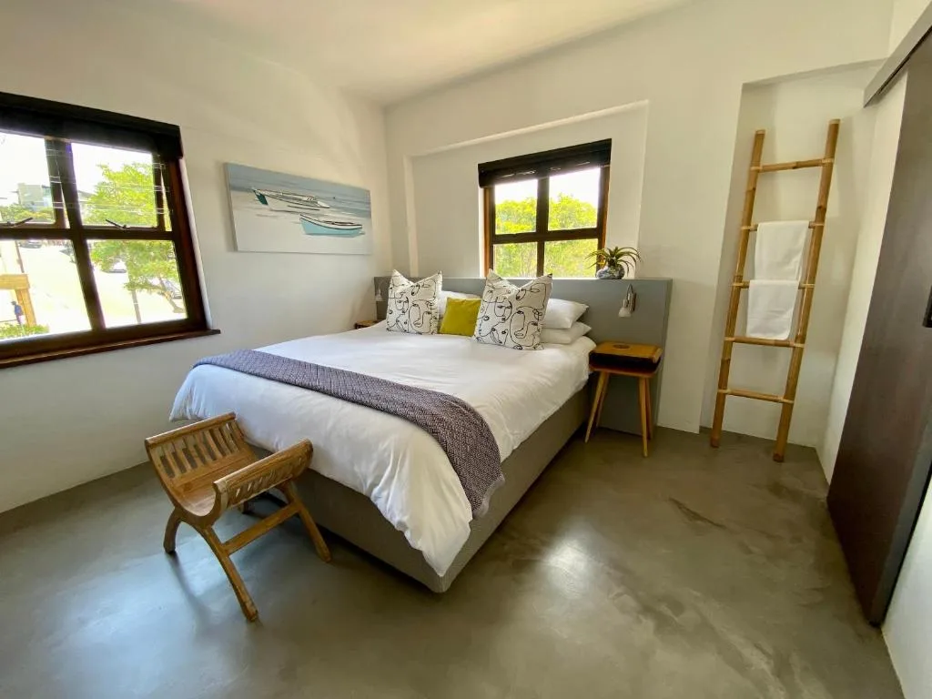 Bright bedroom with queen bed, wooden furniture, and large windows overlooking greenery