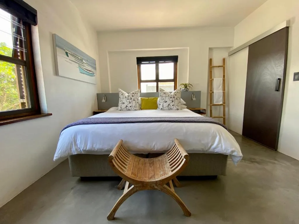 Modern bedroom with neatly made bed, wooden bench, and natural light from window