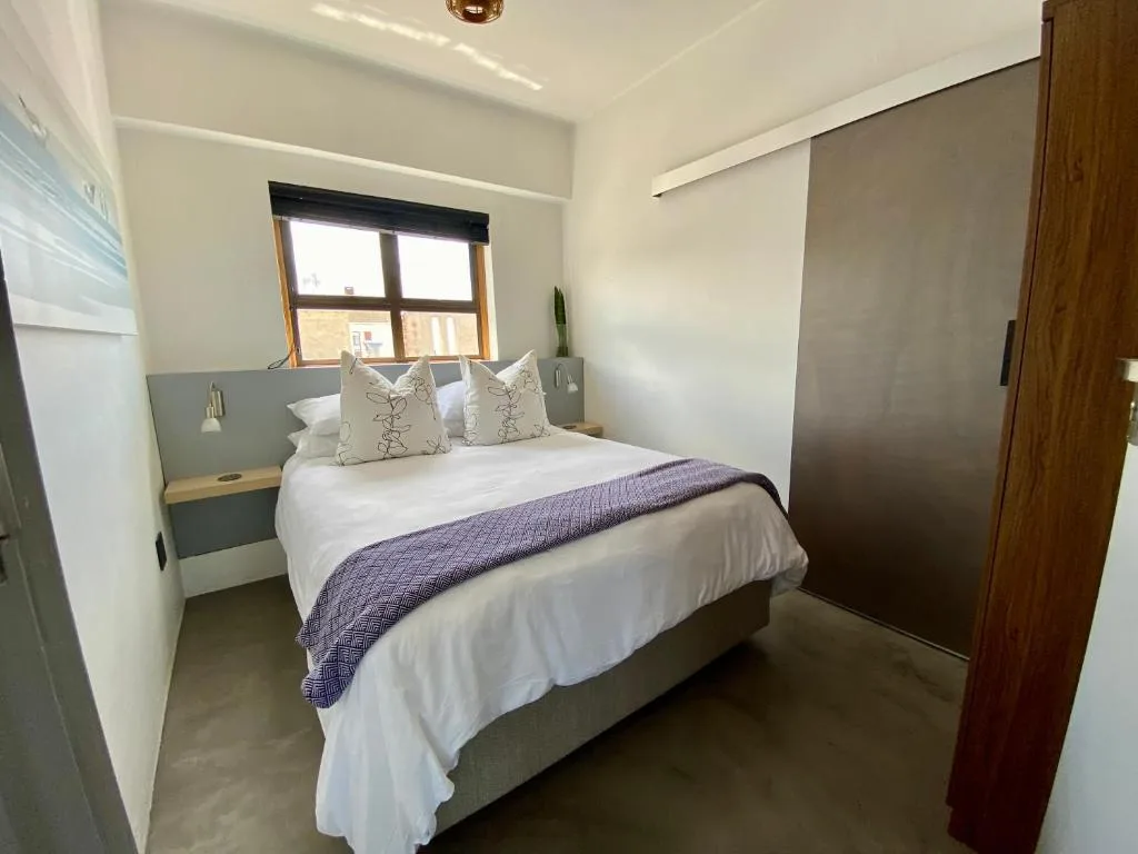 Modern bedroom with queen bed, white linens, and natural light from window