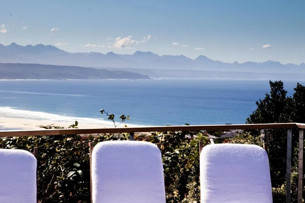 Panoramic ocean and mountain vista from seaside deck with white cushioned seating