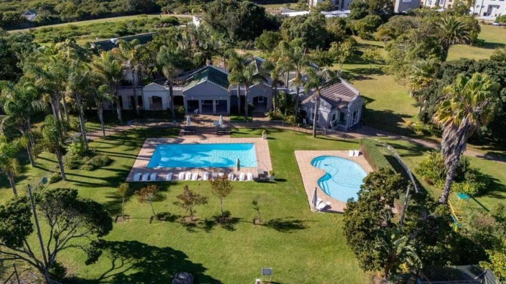 Aerial view of white house with two pools surrounded by manicured gardens and palm trees