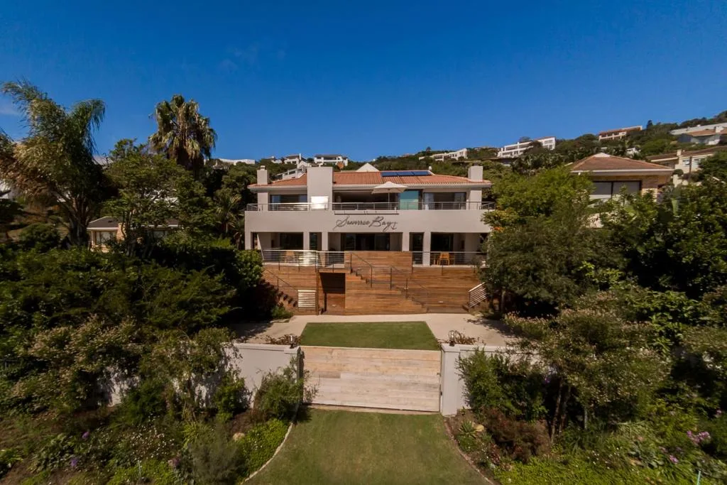 Modern multi-story white building with wooden deck overlooking manicured garden and lawn