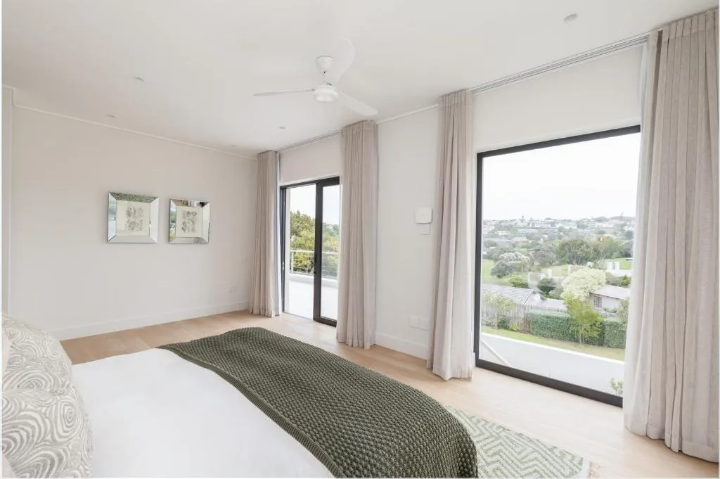 Bright bedroom with bed, glass doors opening to garden views and landscape