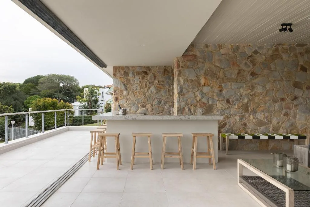 Modern outdoor deck with bar seating and stone fireplace overlooking gardens