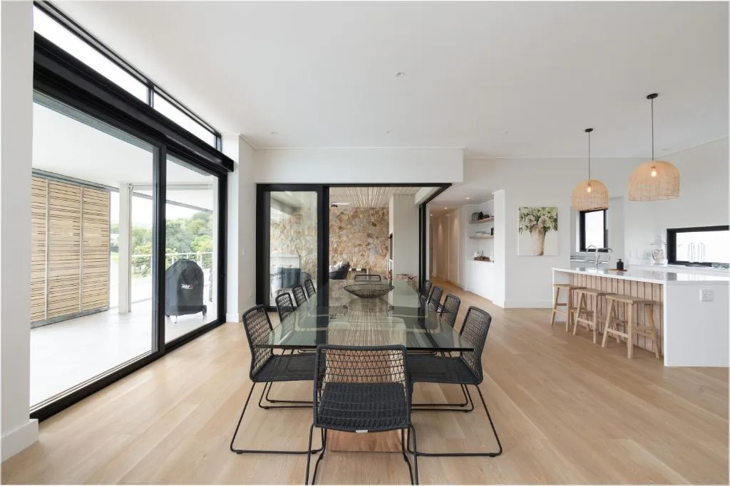 Modern dining area with black table, woven chairs, and ocean views through large windows