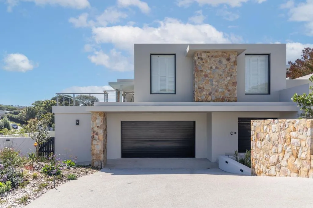 Modern white villa with stone accents and black garage doors on driveway