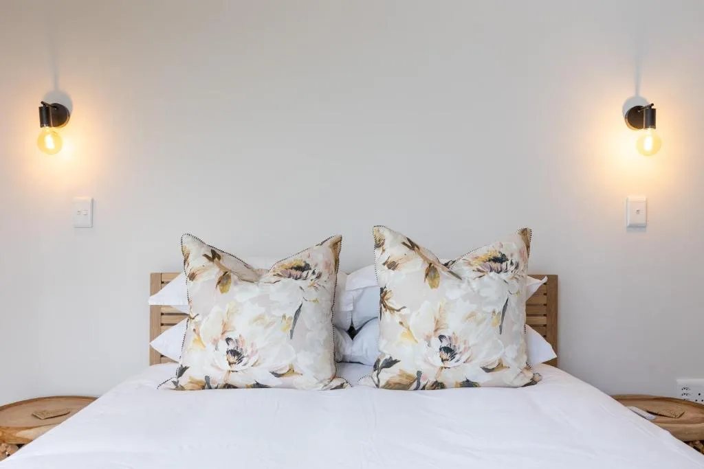Bright bedroom with floral pillows, wooden headboard, and pendant lighting