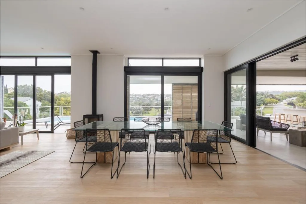 Modern dining area with large table and black chairs overlooking garden views