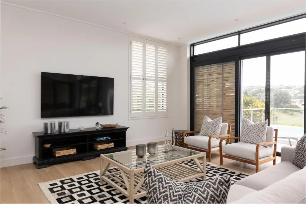 Modern living room with TV, seating, and scenic garden views through large windows