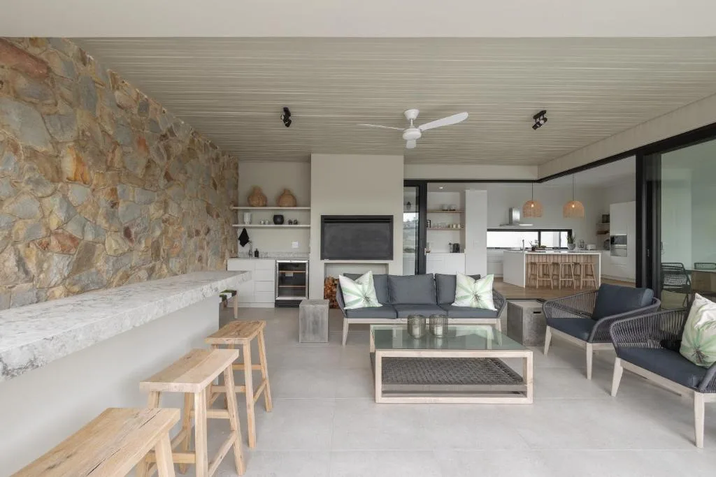 Open-plan lounge with sofa, armchairs, stone fireplace, and kitchen view