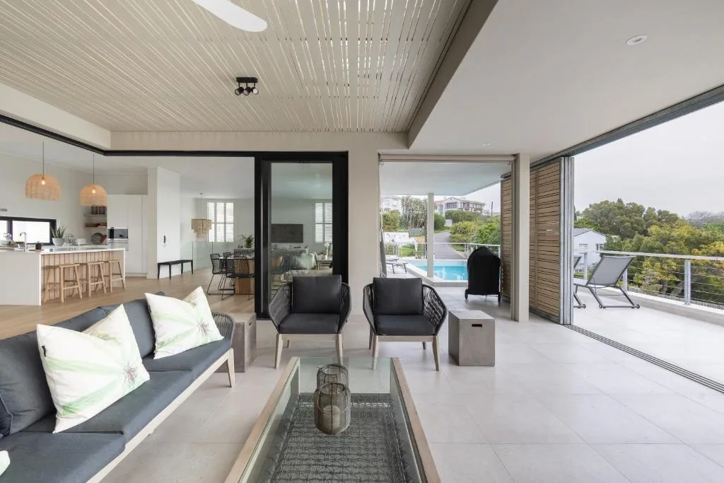 Modern lounge with sofa, chairs, and open views to pool and garden