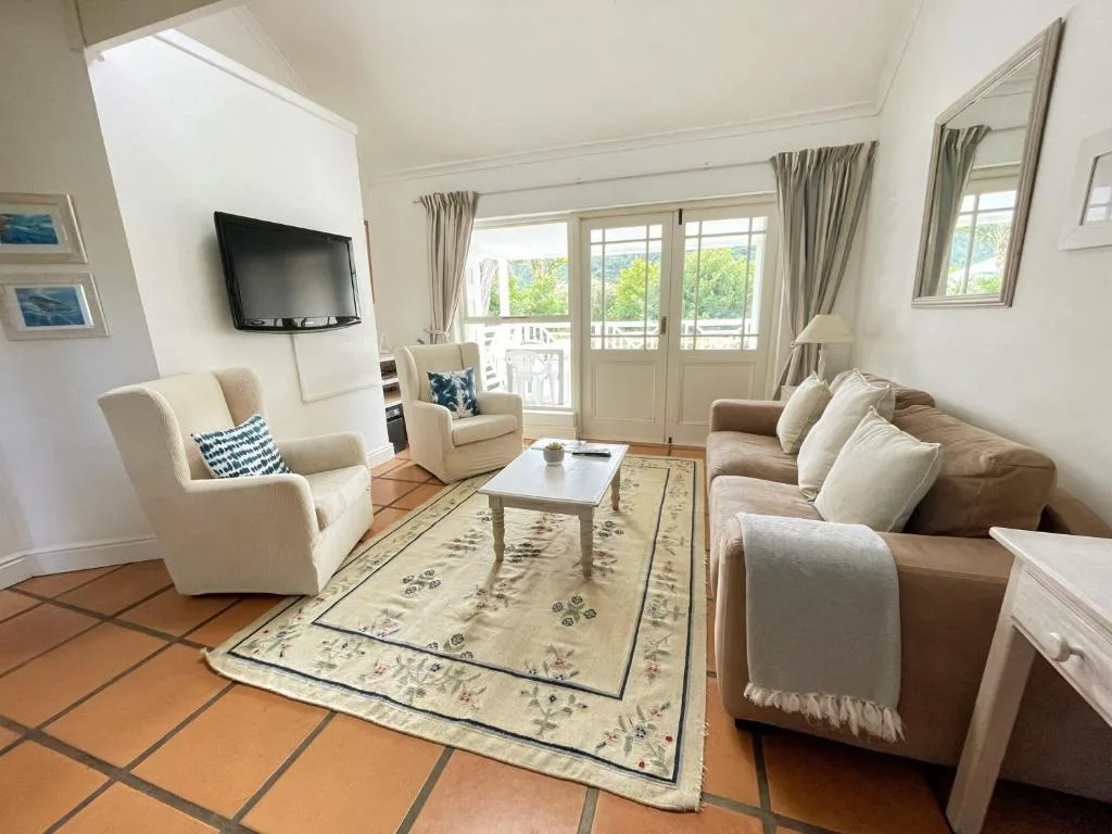 Bright lounge with cream armchairs, sofa, TV, and garden views through glass doors