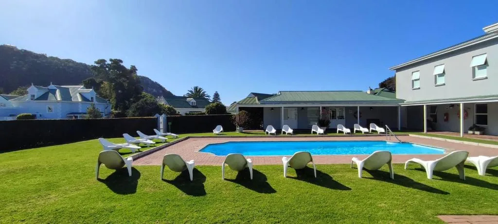 Large swimming pool surrounded by loungers on manicured lawn