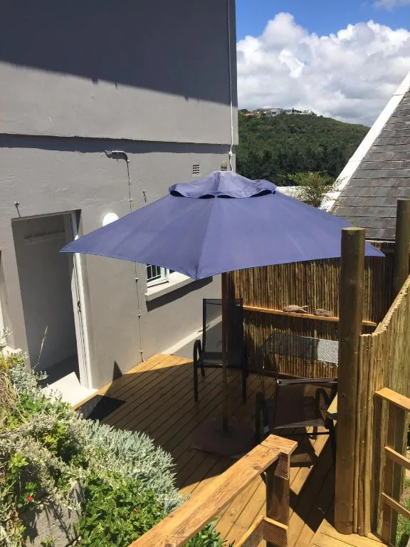 Wooden deck with purple umbrella and chairs overlooking green hills