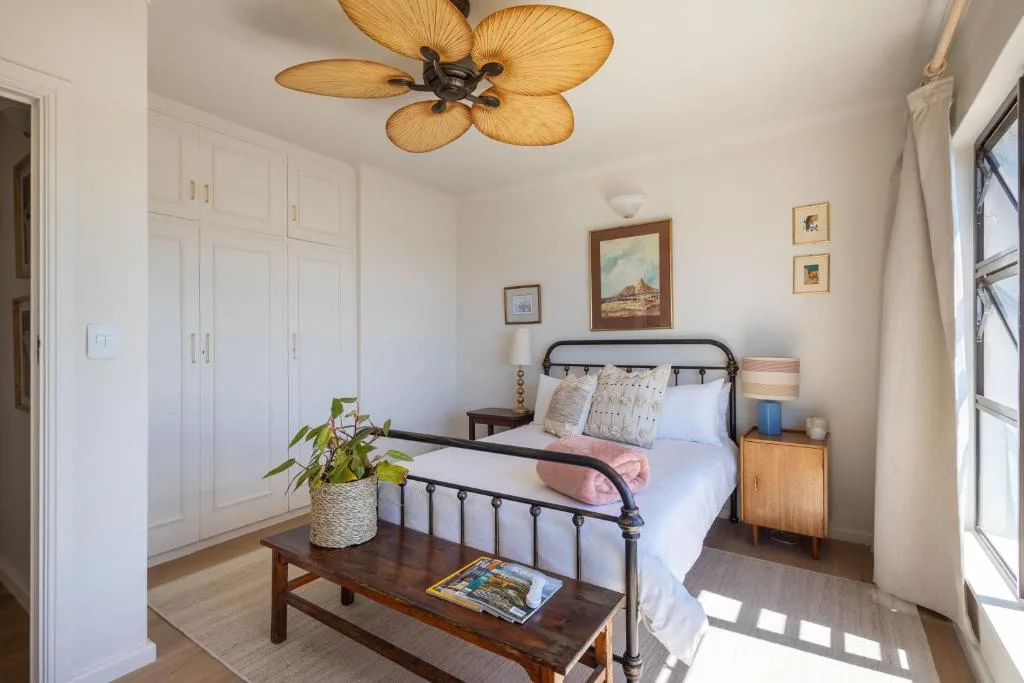 Bright bedroom with metal bed frame, palm ceiling fan, and white built-in wardrobes