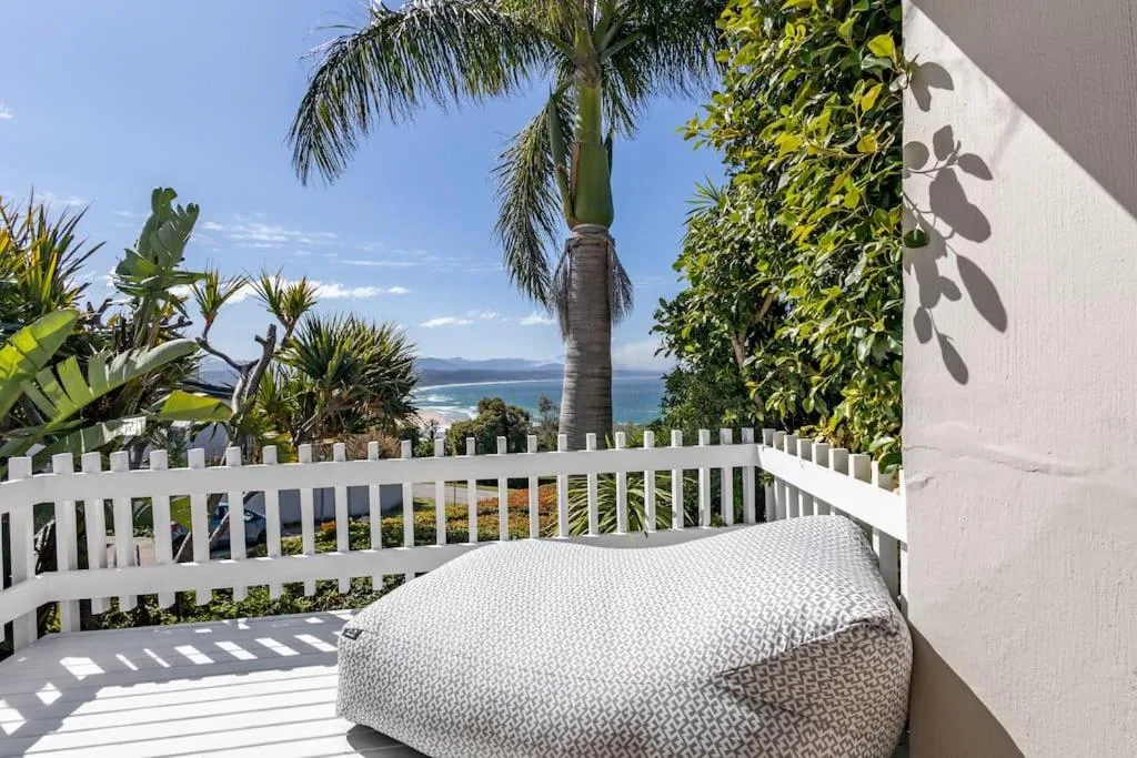 White railed deck with ocean view, tropical plants, and comfortable seating
