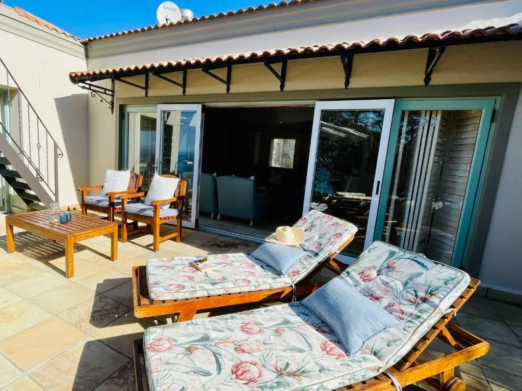 Outdoor patio with wooden loungers, chairs, and covered pergola near villa
