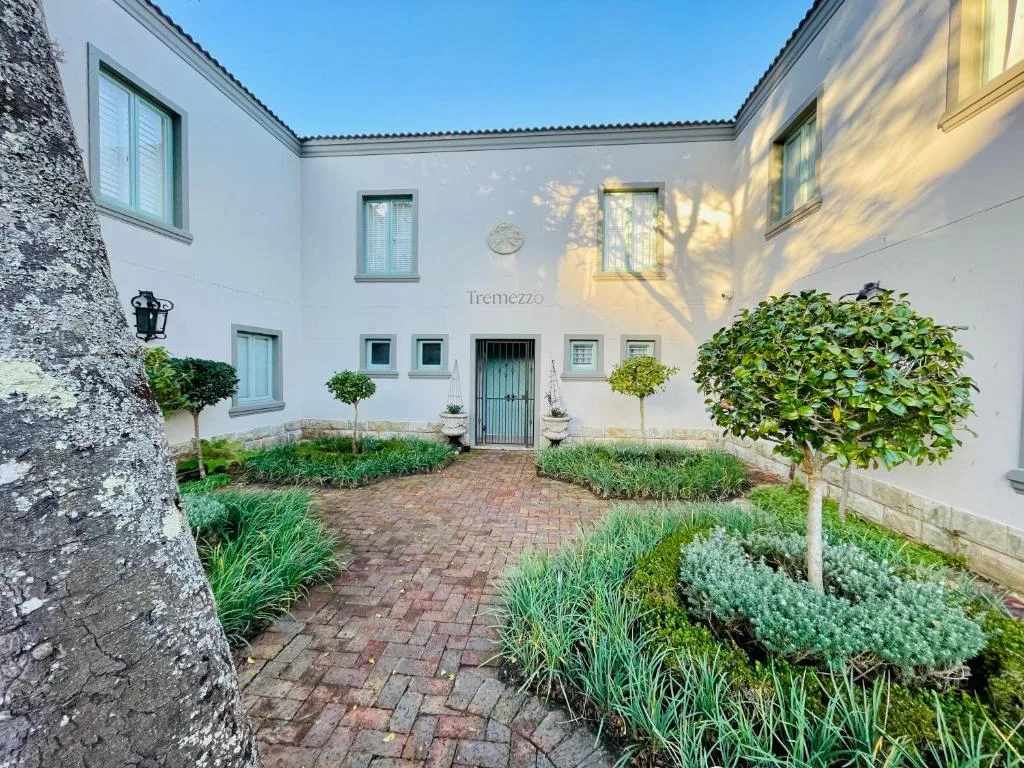 White villa courtyard with brick paving, green door, and manicured landscaping