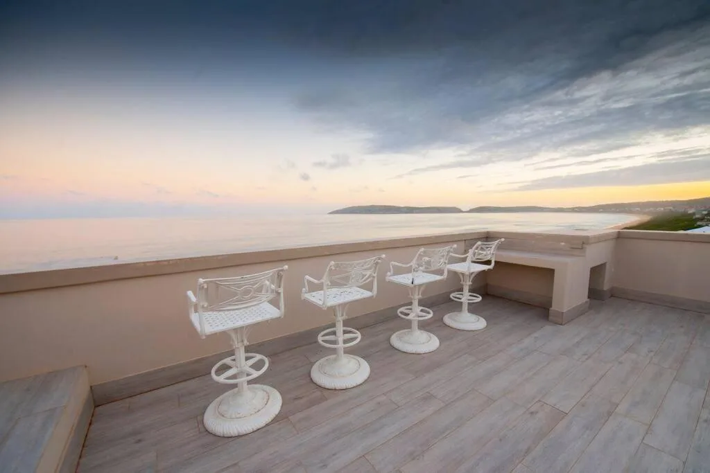 Oceanfront deck with white chairs overlooking Plettenberg Bay at sunset