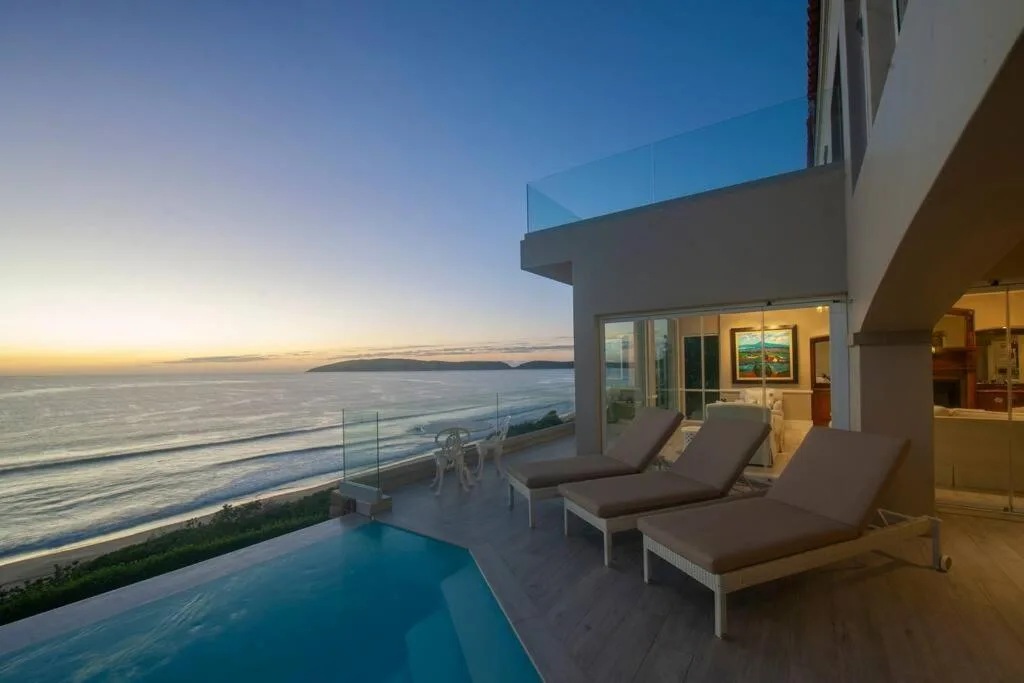 Modern deck with pool, loungers, and ocean views at sunset