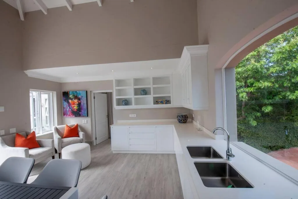 Modern open-plan kitchen with white cabinetry and double sink overlooking garden