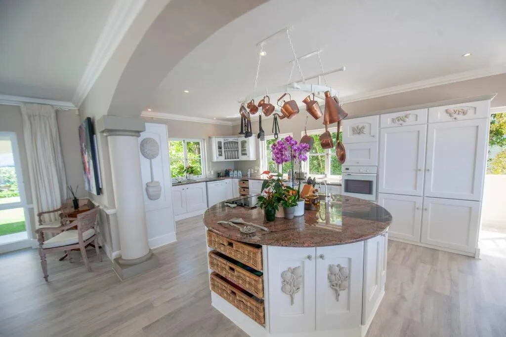 Bright modern kitchen with island, copper pan rack, white cabinetry, and garden views