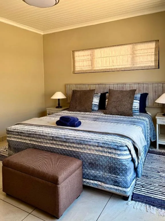Bright bedroom with queen bed, blue bedding, brown pillows, and bedside lamps