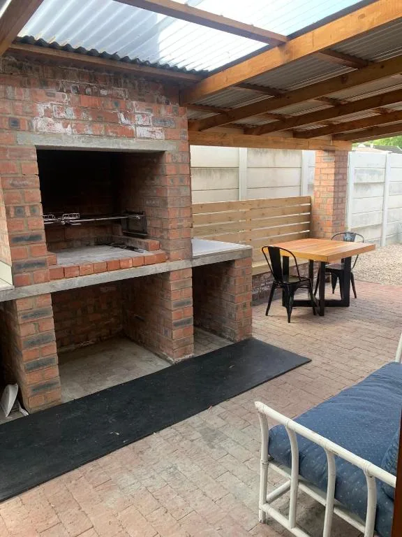 Covered outdoor braai area with brick fireplace and wooden dining table