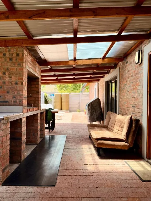 Covered brick patio with wooden beams, seating, and braai area