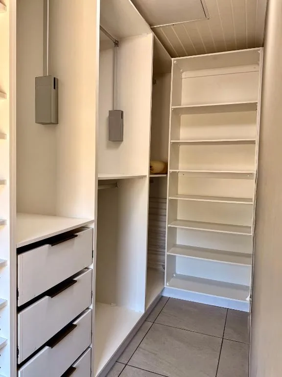 Modern walk-in closet with built-in shelving and white drawers