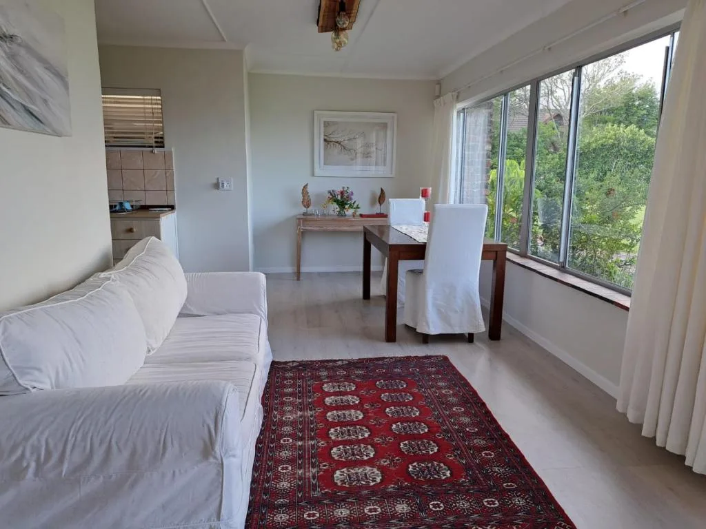 Bright studio lounge with white sofa, dining table, and garden views