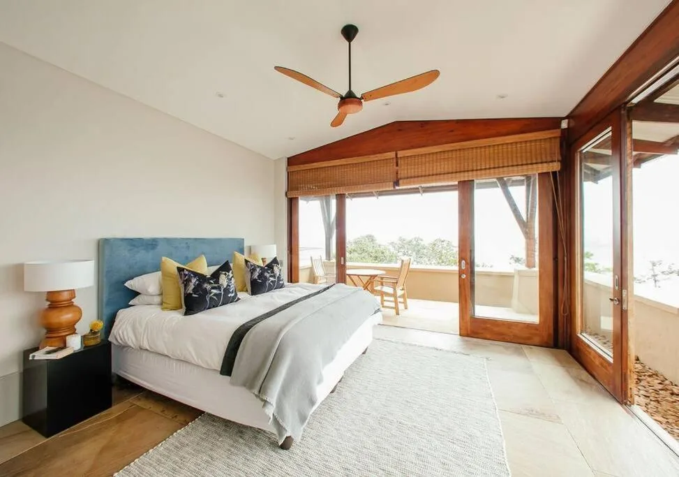 Spacious bedroom with blue headboard, white bedding, and wooden deck access